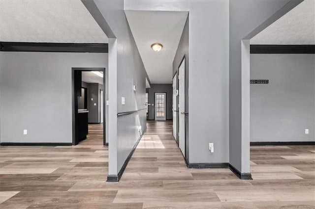 hall with a textured ceiling, crown molding, light wood-style flooring, and baseboards