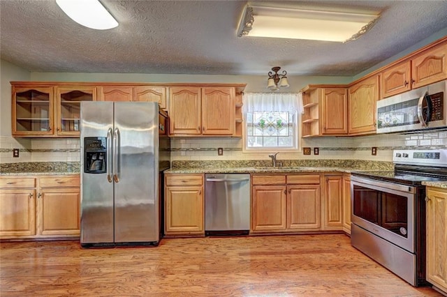 kitchen with a sink, open shelves, stainless steel appliances, and light wood-type flooring