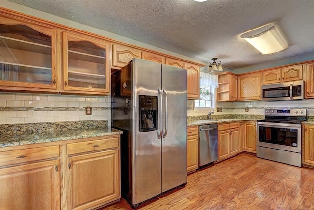 kitchen featuring tasteful backsplash, open shelves, glass insert cabinets, stainless steel appliances, and light wood-style flooring