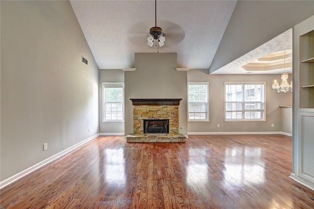 unfurnished living room with a stone fireplace, ceiling fan with notable chandelier, baseboards, wood finished floors, and vaulted ceiling