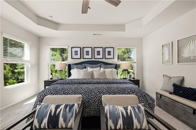 carpeted bedroom featuring multiple windows, ceiling fan, and a tray ceiling