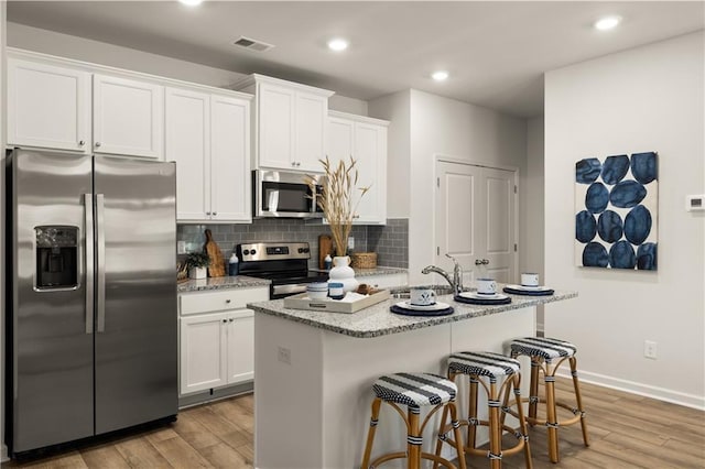 kitchen with white cabinetry, stainless steel appliances, a kitchen island with sink, and light hardwood / wood-style flooring