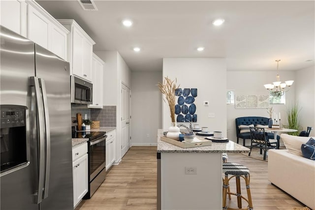 kitchen with stainless steel appliances, white cabinetry, a kitchen island, and a kitchen bar