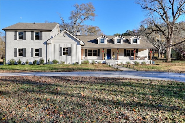 view of front facade featuring brick siding, a porch, a front lawn, and board and batten siding