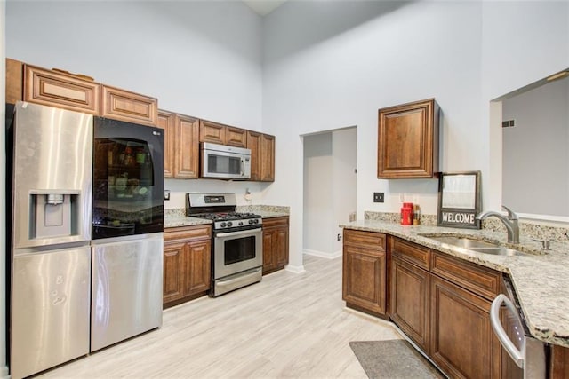 468 Berkshire Pl, Fairburn, GA 30213 - kitchen featuring appliances with stainless steel finishes, a sink, a towering ceiling, light stone counters, and brown cabinetry