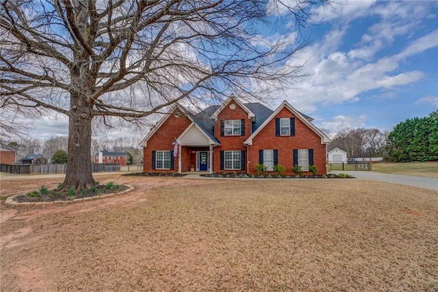 traditional-style house with brick siding, a front lawn, and fence