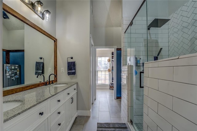 full bath with double vanity, a stall shower, a sink, baseboards, and tile patterned floors