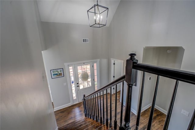 staircase with visible vents, an inviting chandelier, wood finished floors, high vaulted ceiling, and baseboards