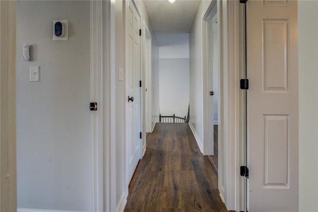 hall featuring dark wood-style floors, a textured ceiling, and baseboards