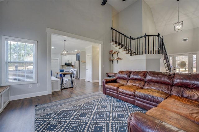 living area with baseboards, visible vents, dark wood-style flooring, stairs, and high vaulted ceiling