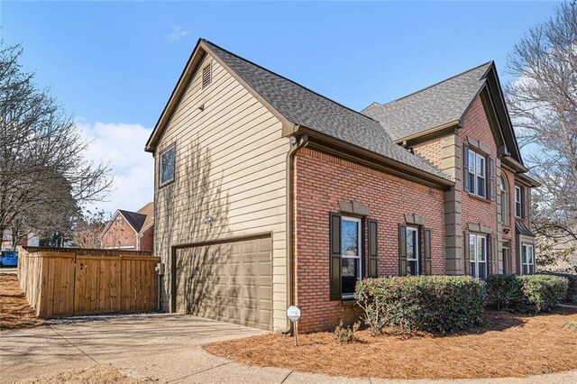 view of property exterior featuring brick siding, a shingled roof, an attached garage, fence, and driveway