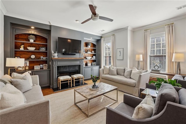 living area with built in features, visible vents, a fireplace, and crown molding