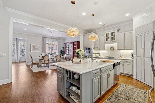 kitchen featuring a center island with sink, stainless steel appliances, gray cabinetry, dark wood-type flooring, and ornamental molding