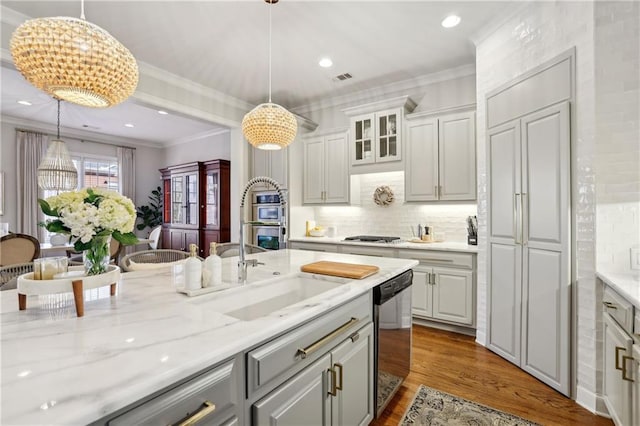 kitchen featuring dishwashing machine, wood finished floors, hanging light fixtures, ornamental molding, and glass insert cabinets