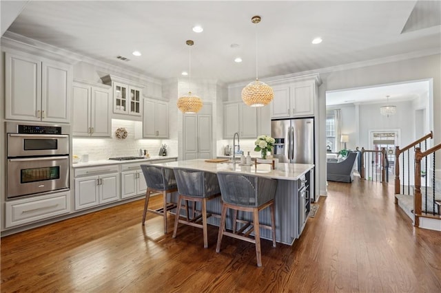 kitchen with a breakfast bar area, stainless steel appliances, tasteful backsplash, visible vents, and ornamental molding