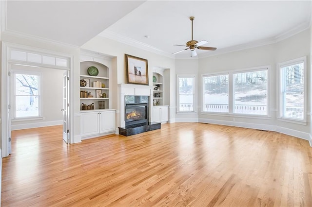 unfurnished living room with built in shelves, a high end fireplace, ornamental molding, and light hardwood / wood-style floors