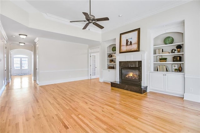 unfurnished living room featuring crown molding, built in features, a high end fireplace, and light hardwood / wood-style flooring