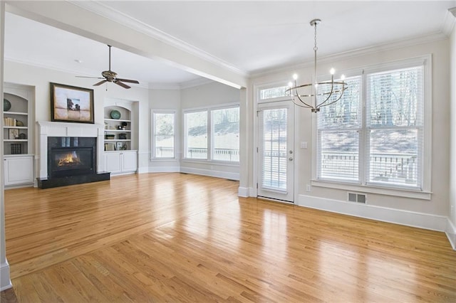 unfurnished living room featuring built in shelves, crown molding, ceiling fan with notable chandelier, and light hardwood / wood-style flooring