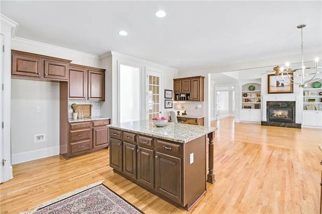 kitchen with decorative light fixtures, light wood-type flooring, ornamental molding, a kitchen island, and light stone countertops