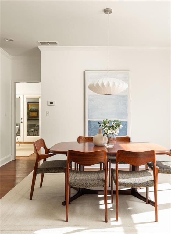 dining space featuring wood finished floors, visible vents, and crown molding