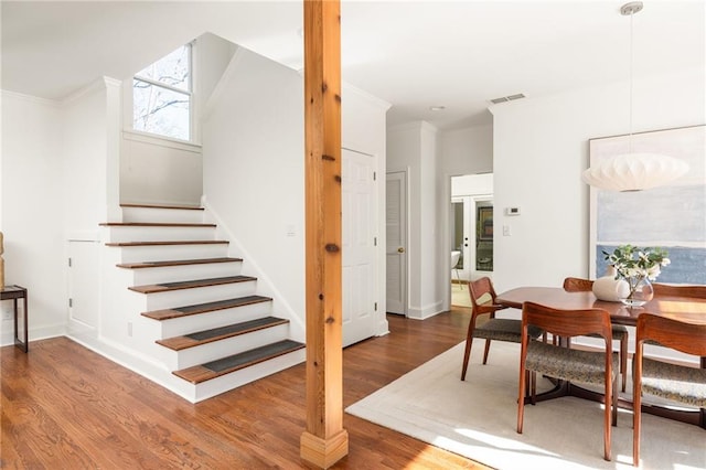 stairway with baseboards, visible vents, ornamental molding, and wood finished floors