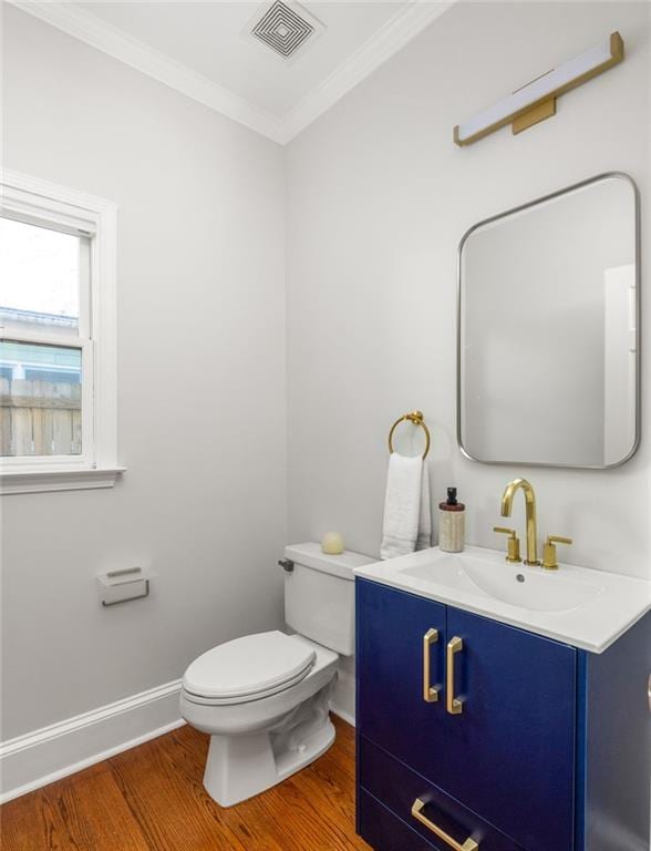 half bath with toilet, visible vents, wood finished floors, and ornamental molding