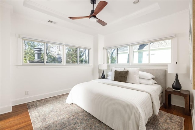 bedroom with a tray ceiling, wood finished floors, visible vents, and baseboards