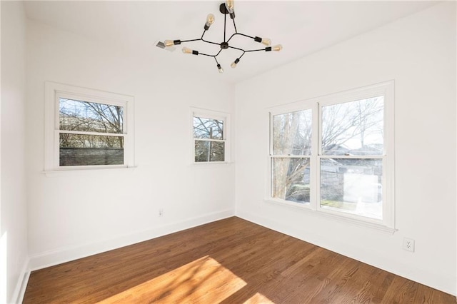 empty room with dark wood-style flooring, a notable chandelier, and baseboards