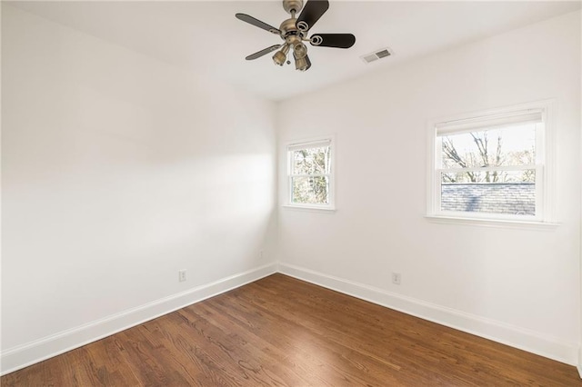 empty room with a ceiling fan, dark wood-style flooring, visible vents, and baseboards