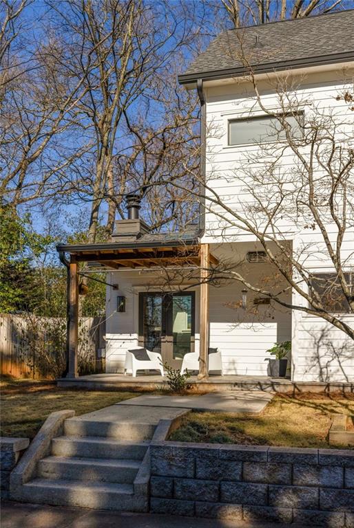 rear view of house featuring a shingled roof and fence