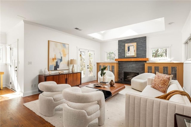 living room with a healthy amount of sunlight, visible vents, wood finished floors, and a stone fireplace