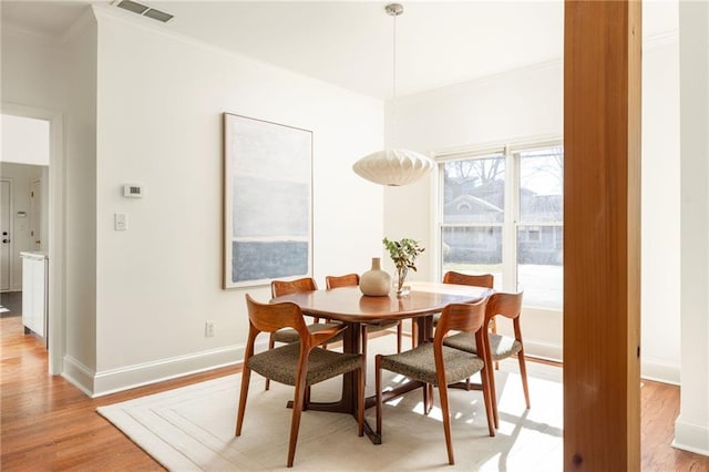 dining area with baseboards, light wood finished floors, visible vents, and crown molding