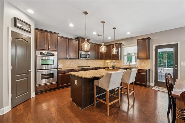kitchen with appliances with stainless steel finishes, dark brown cabinetry, a kitchen island, dark wood-style flooring, and recessed lighting