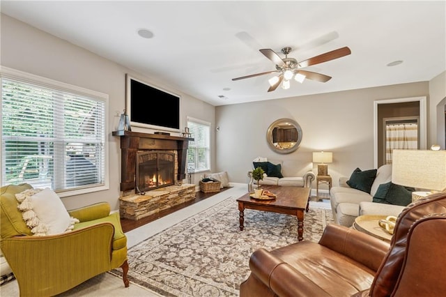living area featuring a stone fireplace, ceiling fan, and carpet flooring