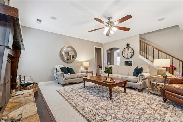 living area featuring ceiling fan, stairs, arched walkways, a fireplace, and carpet flooring