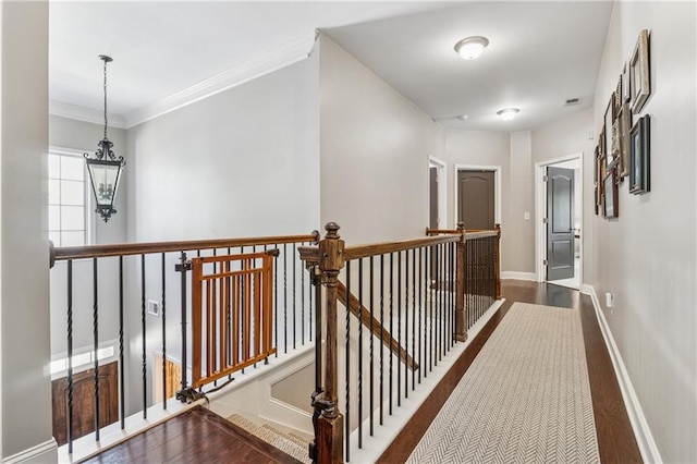 hall with an upstairs landing, baseboards, wood finished floors, a chandelier, and crown molding