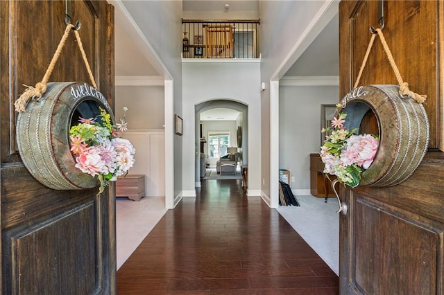 entryway with wood finished floors, arched walkways, ornamental molding, a high ceiling, and baseboards