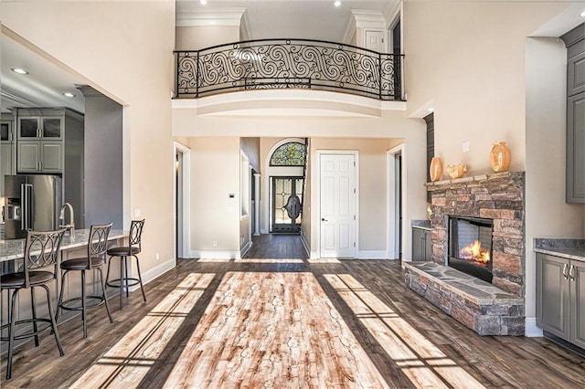 foyer with crown molding, a stone fireplace, dark wood-type flooring, and a high ceiling