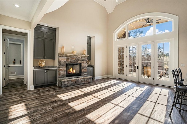 unfurnished living room with french doors, ornamental molding, ceiling fan, dark wood-type flooring, and a fireplace