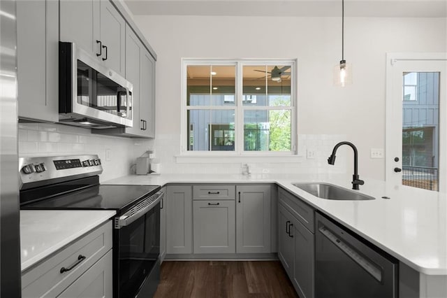 kitchen with dark wood-style flooring, a peninsula, a sink, appliances with stainless steel finishes, and gray cabinetry
