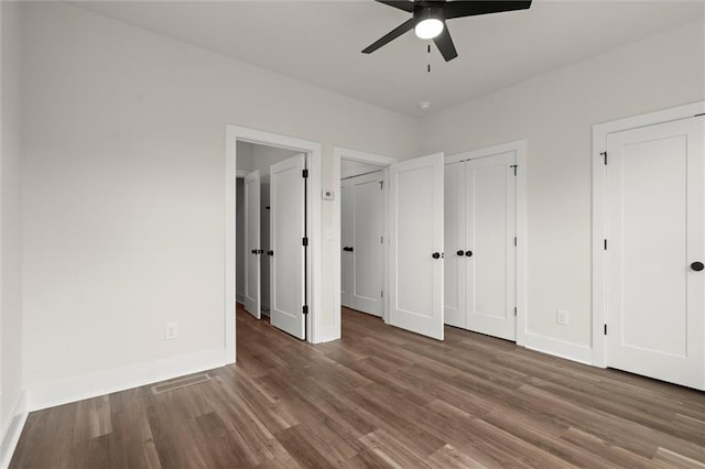 unfurnished bedroom featuring ceiling fan, baseboards, multiple closets, and wood finished floors