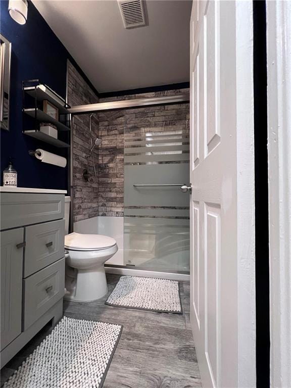 bathroom with hardwood / wood-style flooring, a shower with door, vanity, and toilet