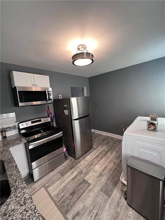 kitchen featuring appliances with stainless steel finishes, washer / clothes dryer, white cabinets, light wood-type flooring, and dark stone counters