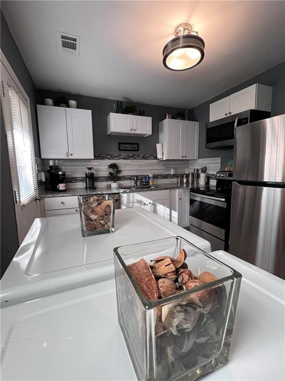 kitchen with decorative backsplash, white cabinetry, and stainless steel appliances