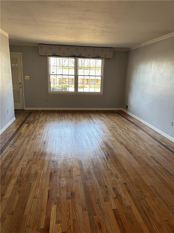 empty room with crown molding, dark wood-style floors, and baseboards