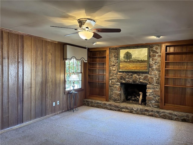unfurnished living room with a fireplace, carpet, wooden walls, and ceiling fan