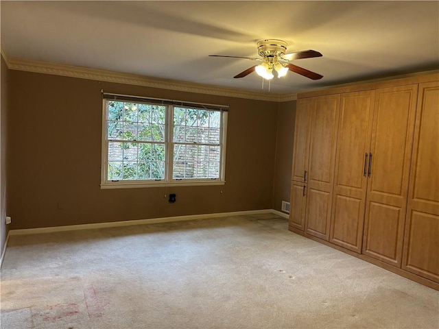 unfurnished bedroom with light colored carpet, baseboards, visible vents, a ceiling fan, and crown molding