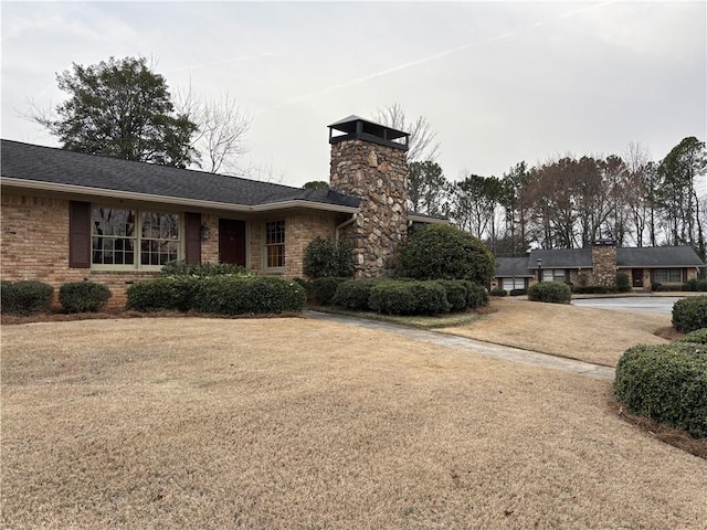 single story home with a chimney, a front yard, and brick siding