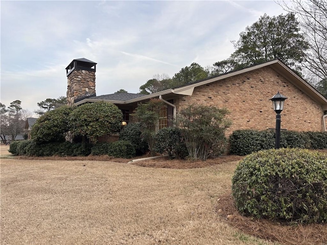 view of side of home featuring a lawn, a chimney, and brick siding
