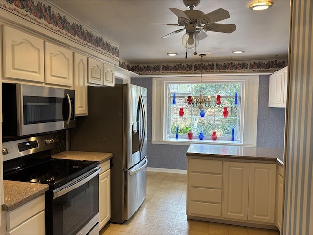 kitchen with light stone counters, wallpapered walls, stainless steel appliances, ceiling fan with notable chandelier, and baseboards